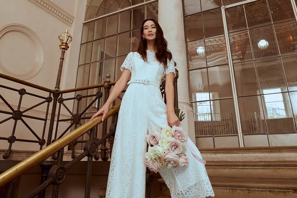 Model wearing a wide leg lace wedding jumpsuit holding a rose bouquet