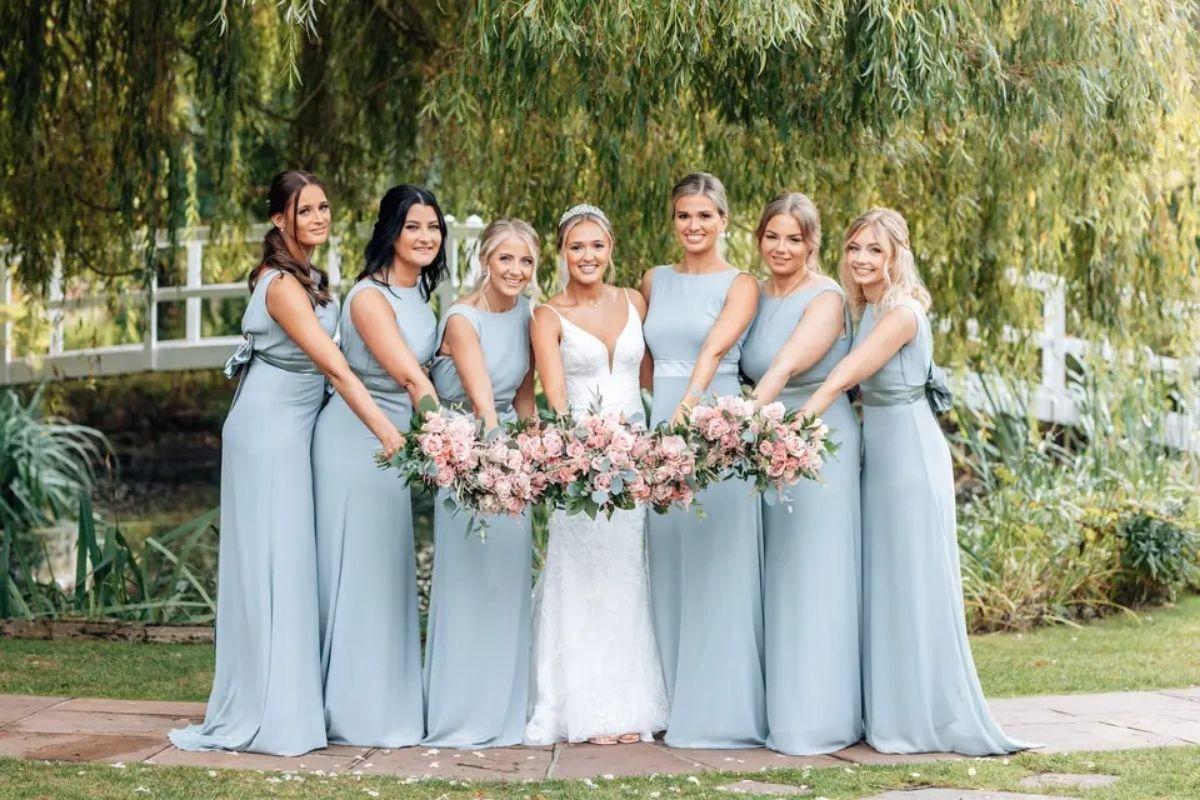 a bride with her six bridesmaids all wearing powder blue bridesmaid dresses holding their wedding bouquets