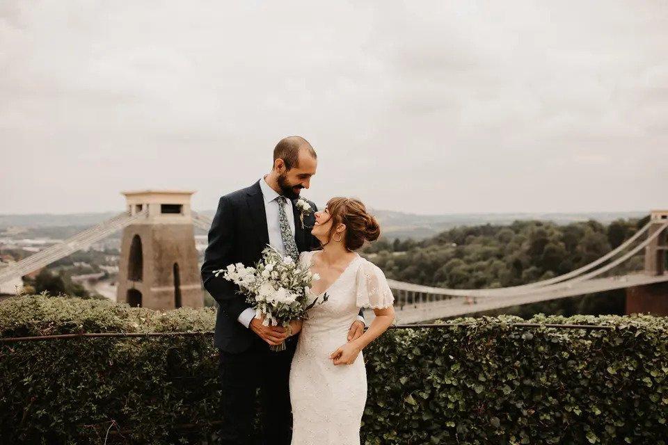 Bride and groom embrace at a viewpoint overlooking the Clifton Suspension Bridge