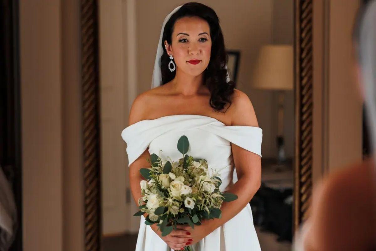a picture of a beautiful brunette bride wearing an off the shoulder white wedding dress, red lipstick and retro hair
