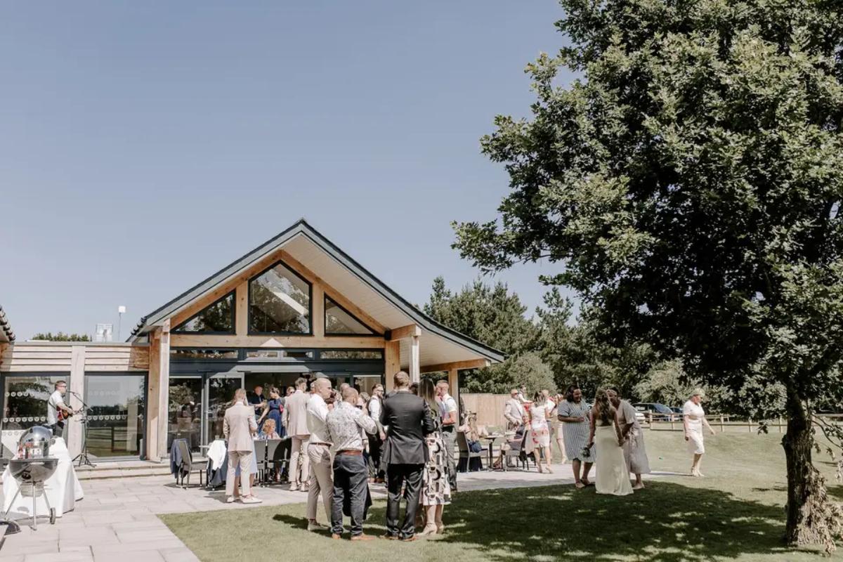 A group of wedding guests standing outside a wooden and glass barn wedding venue in Suffolk