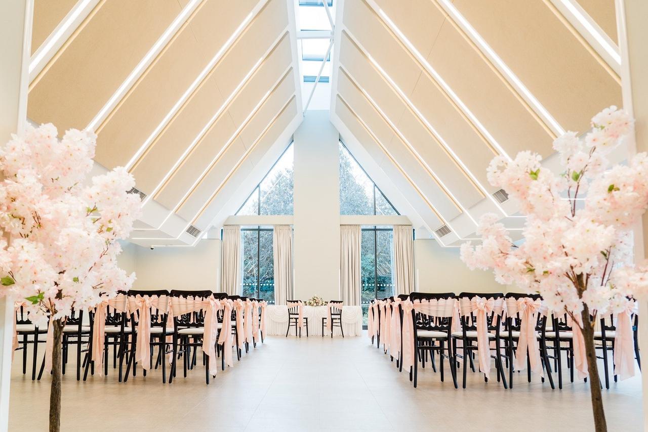 A light, contemporary events space set up for a wedding ceremony with pink cherry blossom trees.