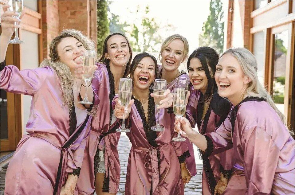 A wedding party wearing matching silk dressing gowns, holding glasses of champagne and smiling at the camera