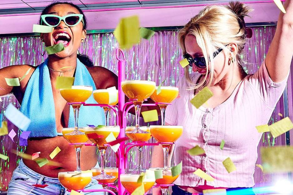 two women partying in a bar on a london hen do with a tower of pornstar martinis in front of them