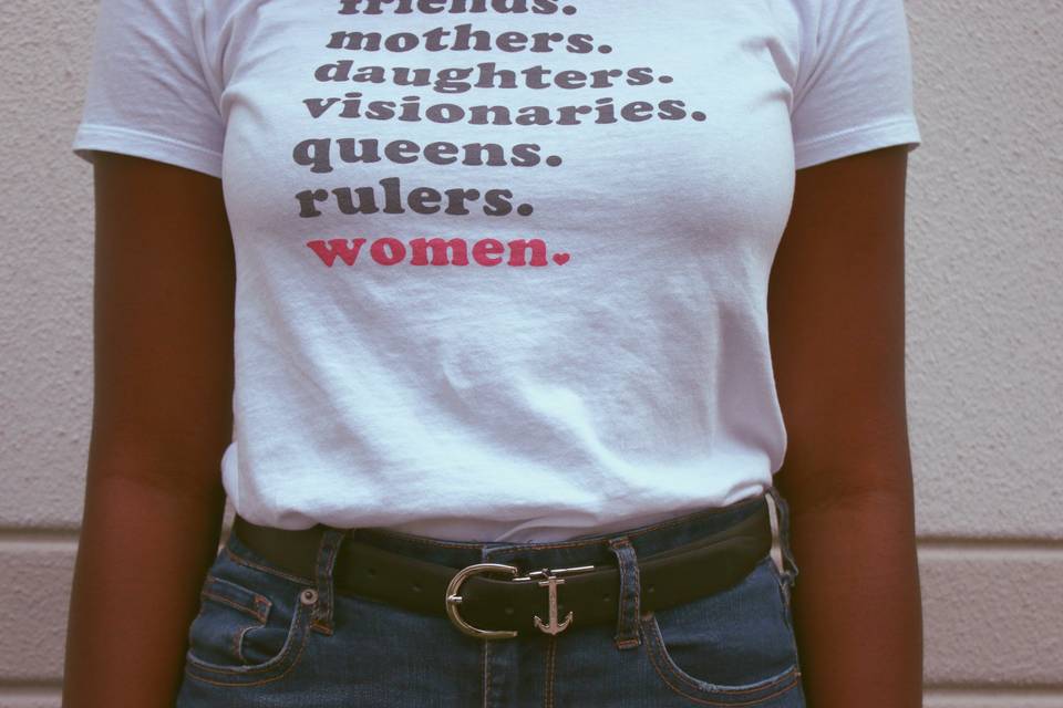 Woman wearing a white t-shirt that says mothers, daughters, visionaries, queens, women