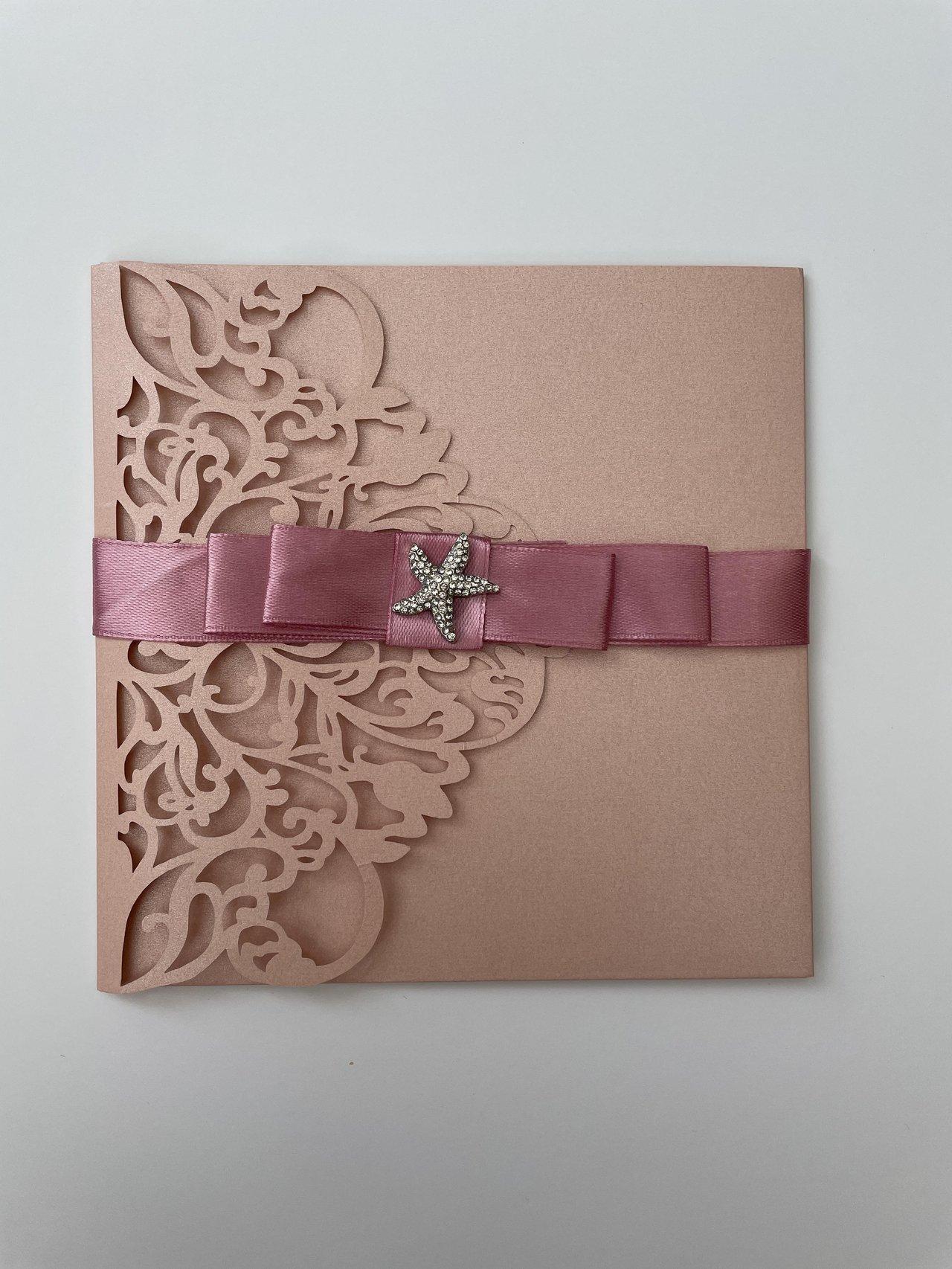 Traditional style laser cut pink wedding invitation with pink ribbon and a sparkly starfish detail