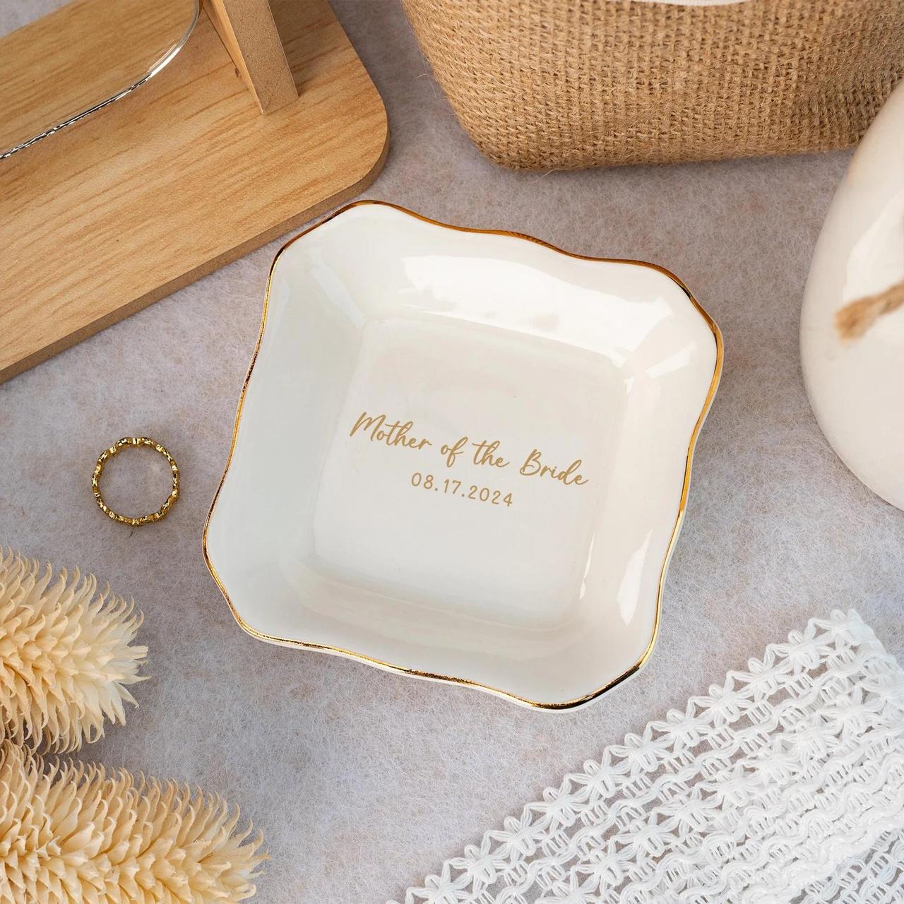 A white and gold ceramic ring dish that reads 'mother of the bride' and date of wedding.