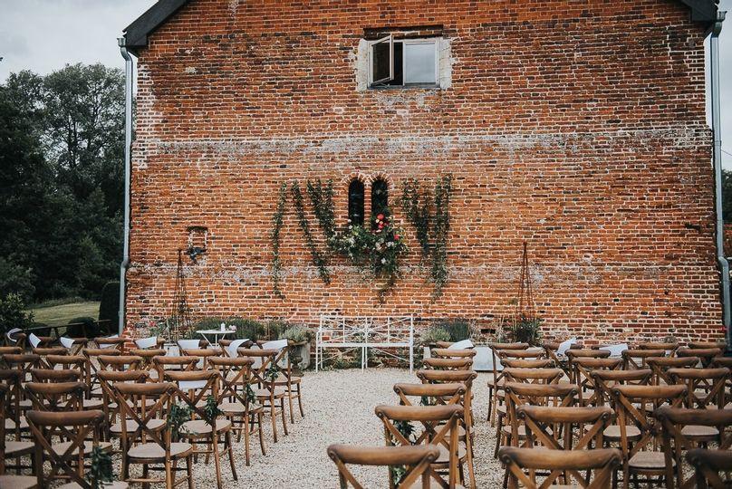 A large brick wall side of a building decorated with vines and a selection of wedding ceremony chairs set up outside