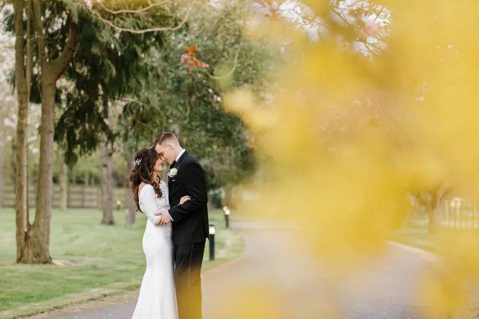 Bride and groom embrace on a driveway surrounded by trees and greenery