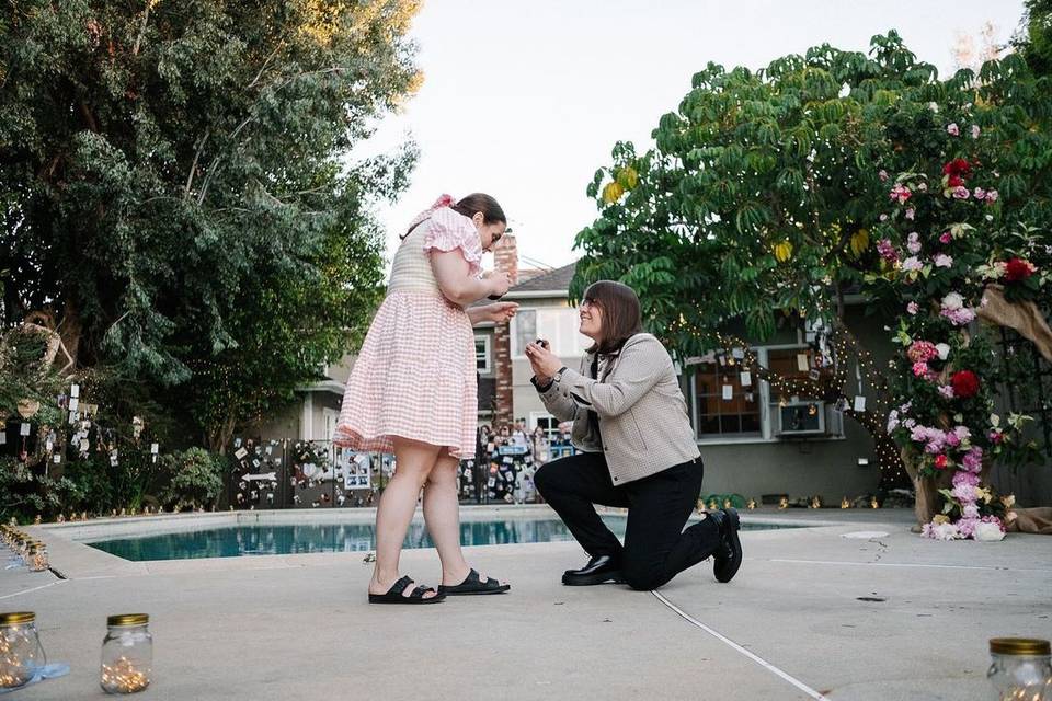 Bonnie Chance on one knee proposing to Beanie Feldstein