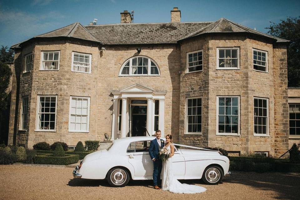 Bride and groom stand outside a country house with a vintage car
