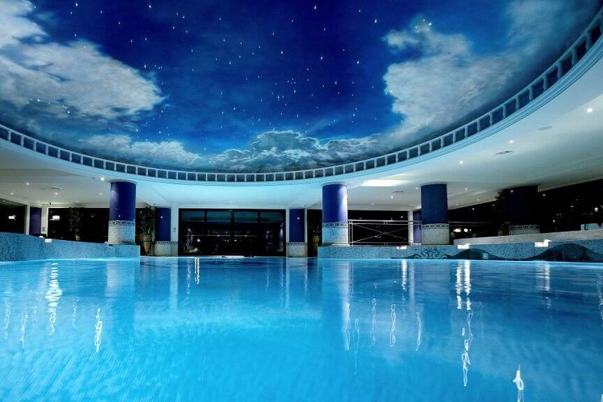 A large blue round swimming pool in a sleek fitness studio surrounded by blue pillars with a large starry skylight up above