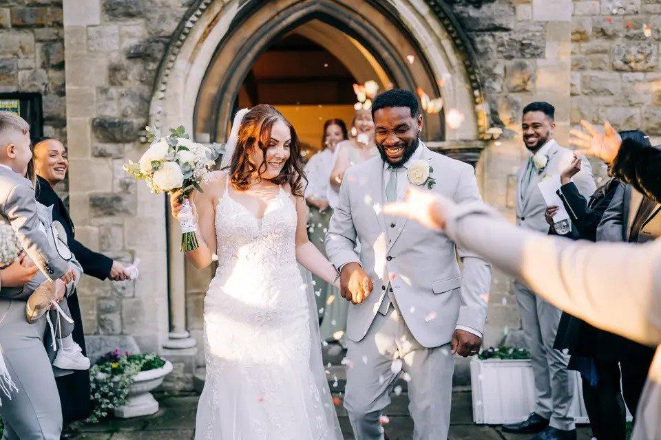 Bride and groom exit church hand-in-hand while guests throw confetti