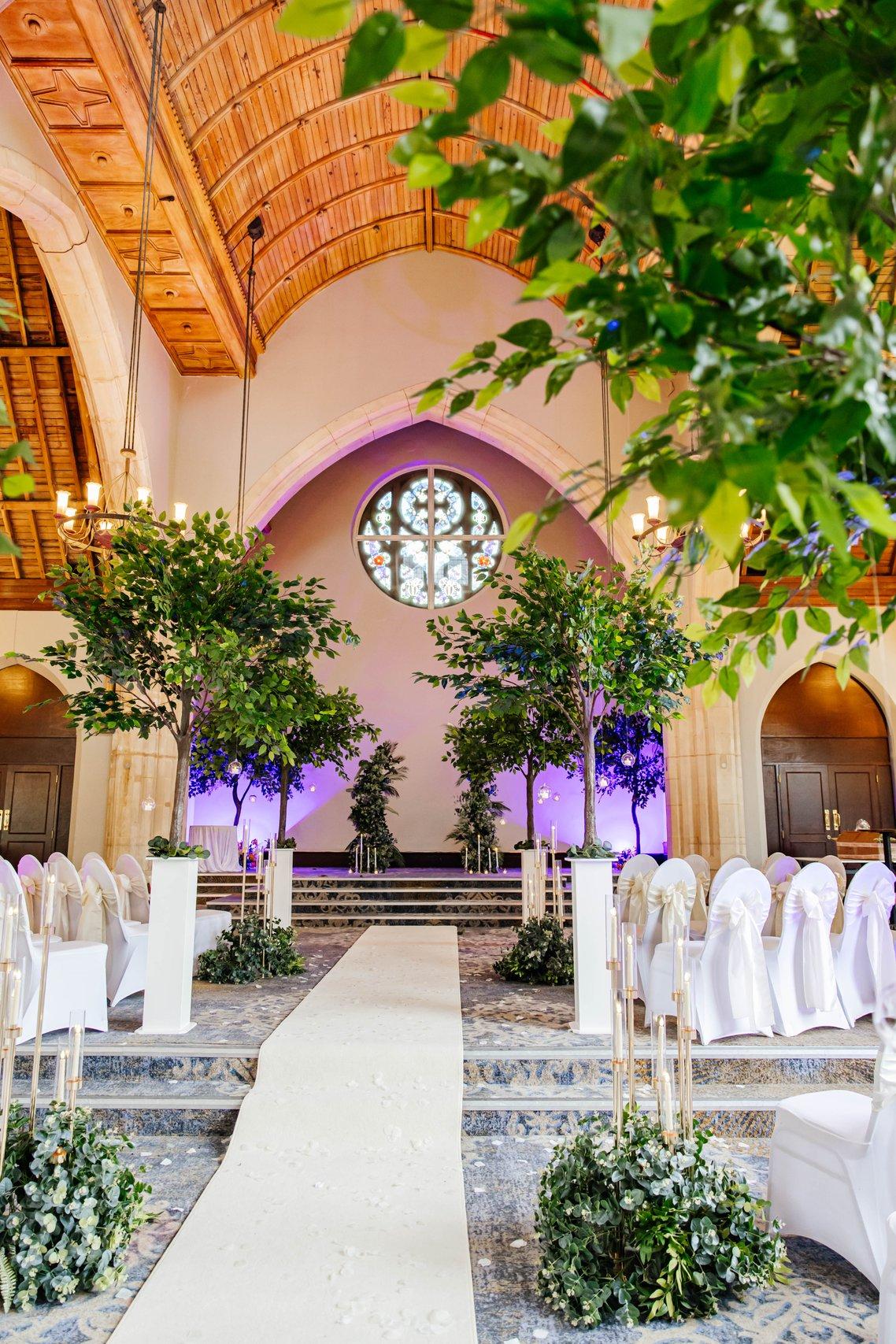 Interior of a converted chapel wedding venue set up for a ceremony with indoor trees and chairs with white covers.