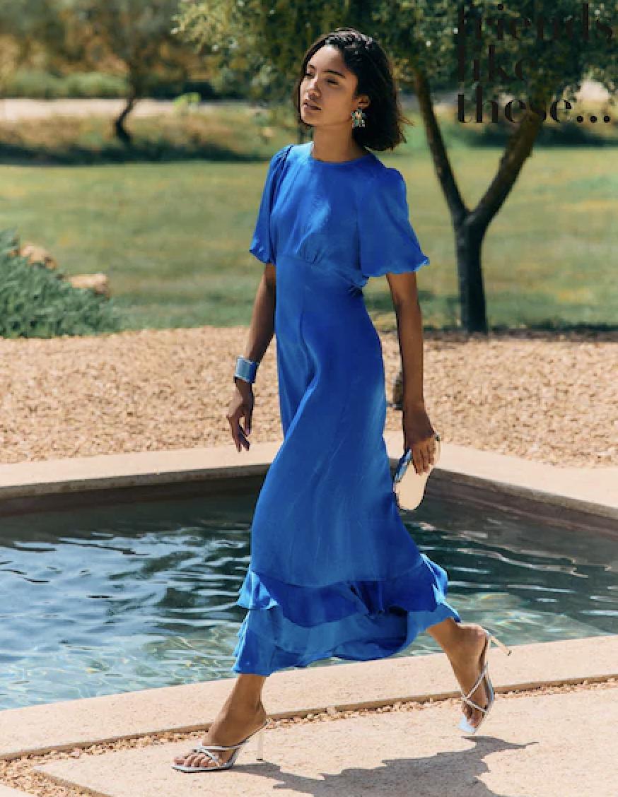 model walking past a swimming pool in a blue ruffled midi dress