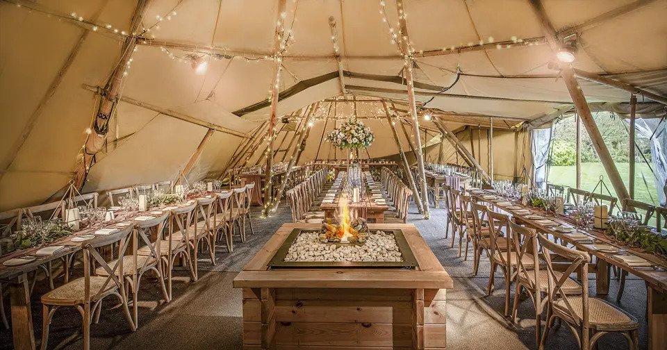 Interior of tipi venue with fire pit, long tables with wooden chairs and fairy lights