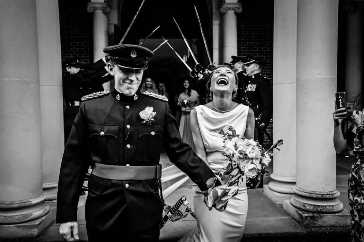 a groom in military wedding attire holding his bride's hand as they laugh and smile walking out of their wedding ceremony