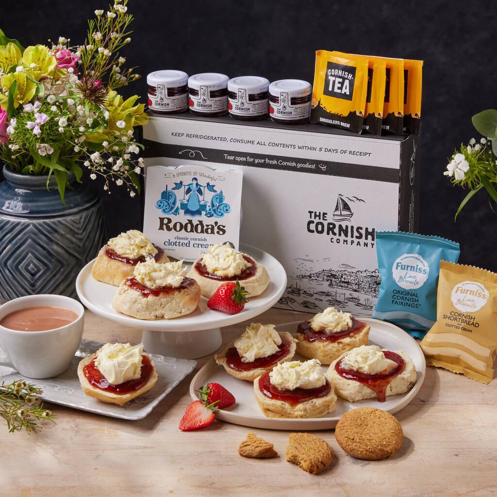 An array of afternoon cream tea goodies including scones with jam and cream, a cup of tea and some packets of biscuits.