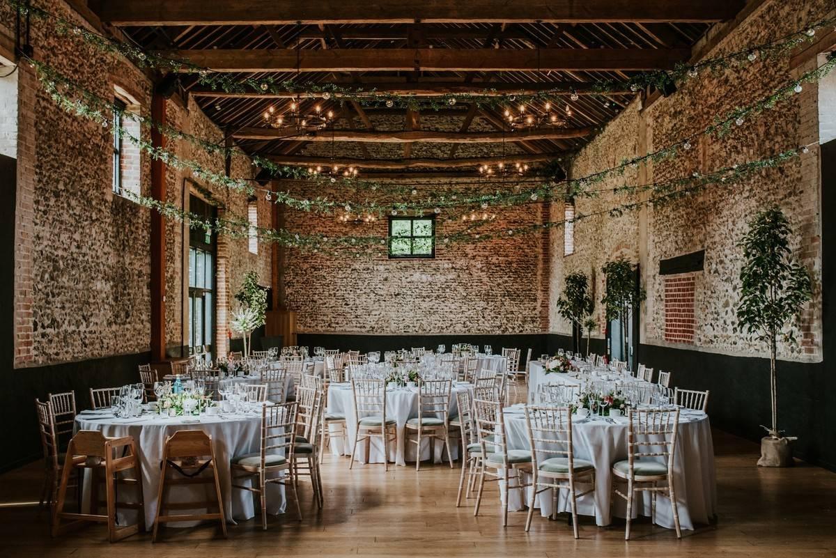 A moody brick built wedding barn set up for a wedding breakfast with charming fairy lights and vines hanging above