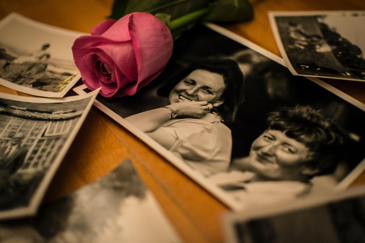 Black and white family photos spread out on a wooden memory table with a bright pink rose over the top