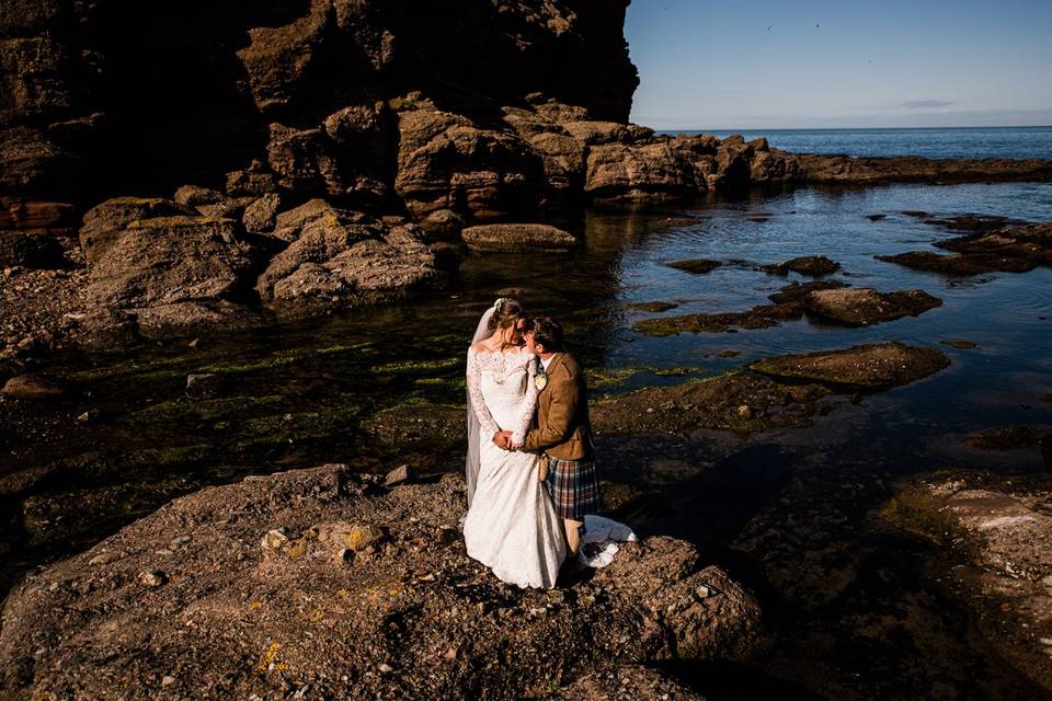 Caitlin and Stephen in wedding outfits on a rocky beach in Scotland