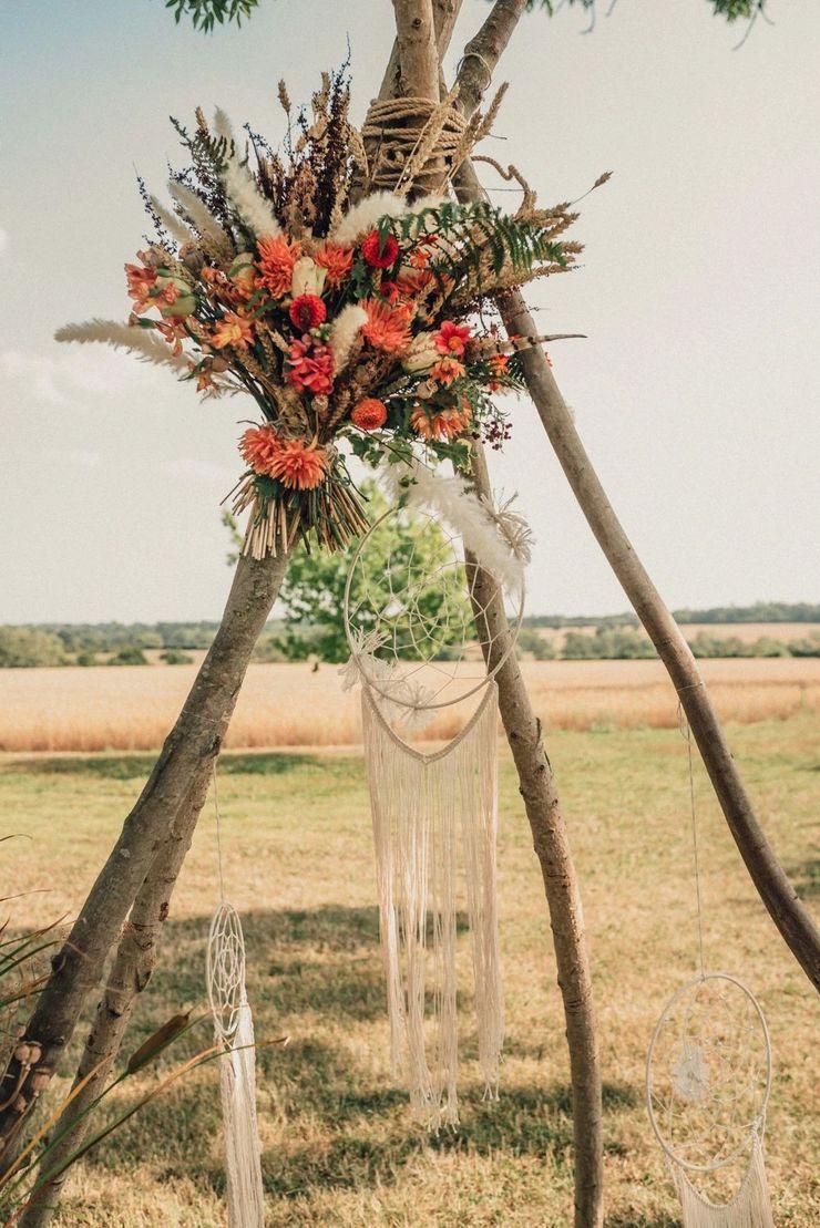 A tipi style arch made of silver birch with a dried flower bouquet at the top left 