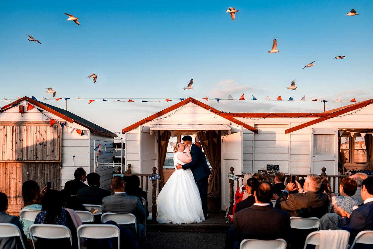 bride and groom kissing at the alter on a beach in front of a white hut