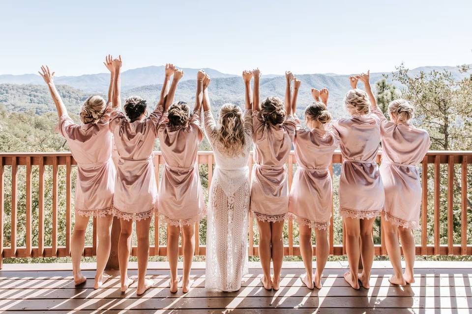 A bride wearing a bride dressing gown with bridesmaids either side of her in matching bridal party robes holding their arms up 