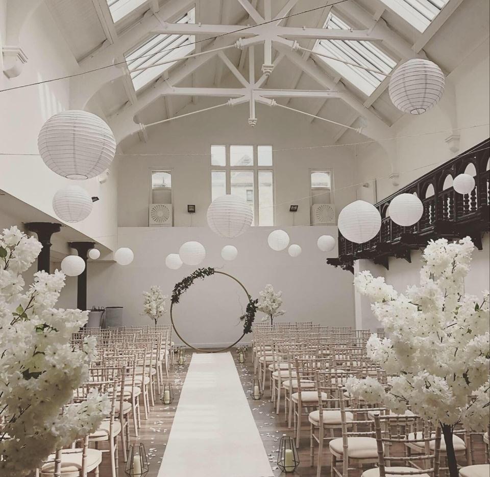 The interior of a white-washed, modern wedding venue with Victorian period touches such as high ceilings and ornate plasterwork. It is set up for a civil ceremony.