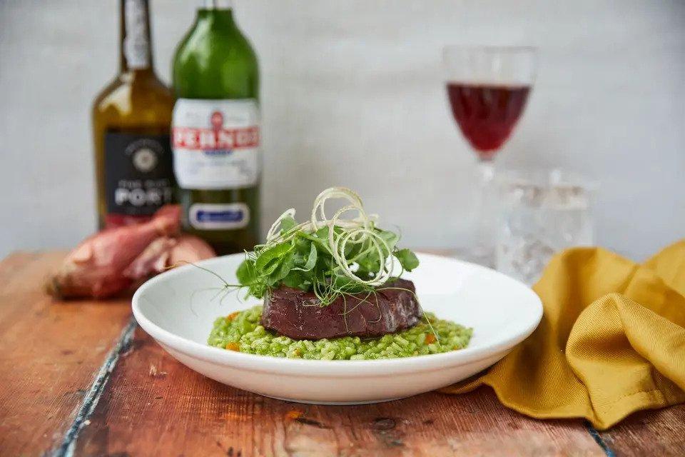 Risotto topped with meat and green staged with liquor and a glass of red wine