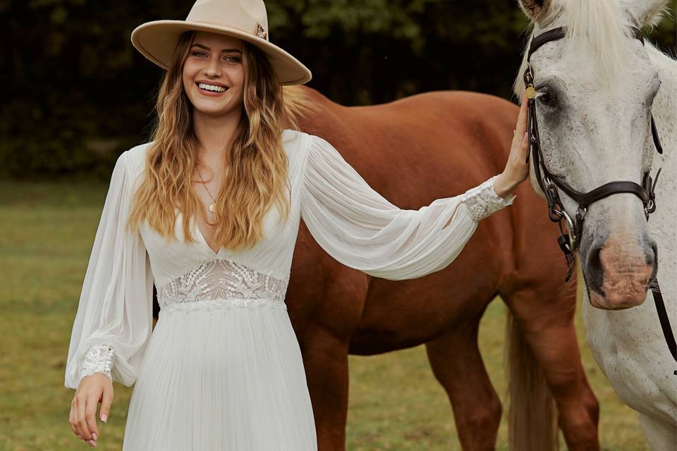 Boho bride in a wide brim hat and a bohemian wedding dress next to a horse