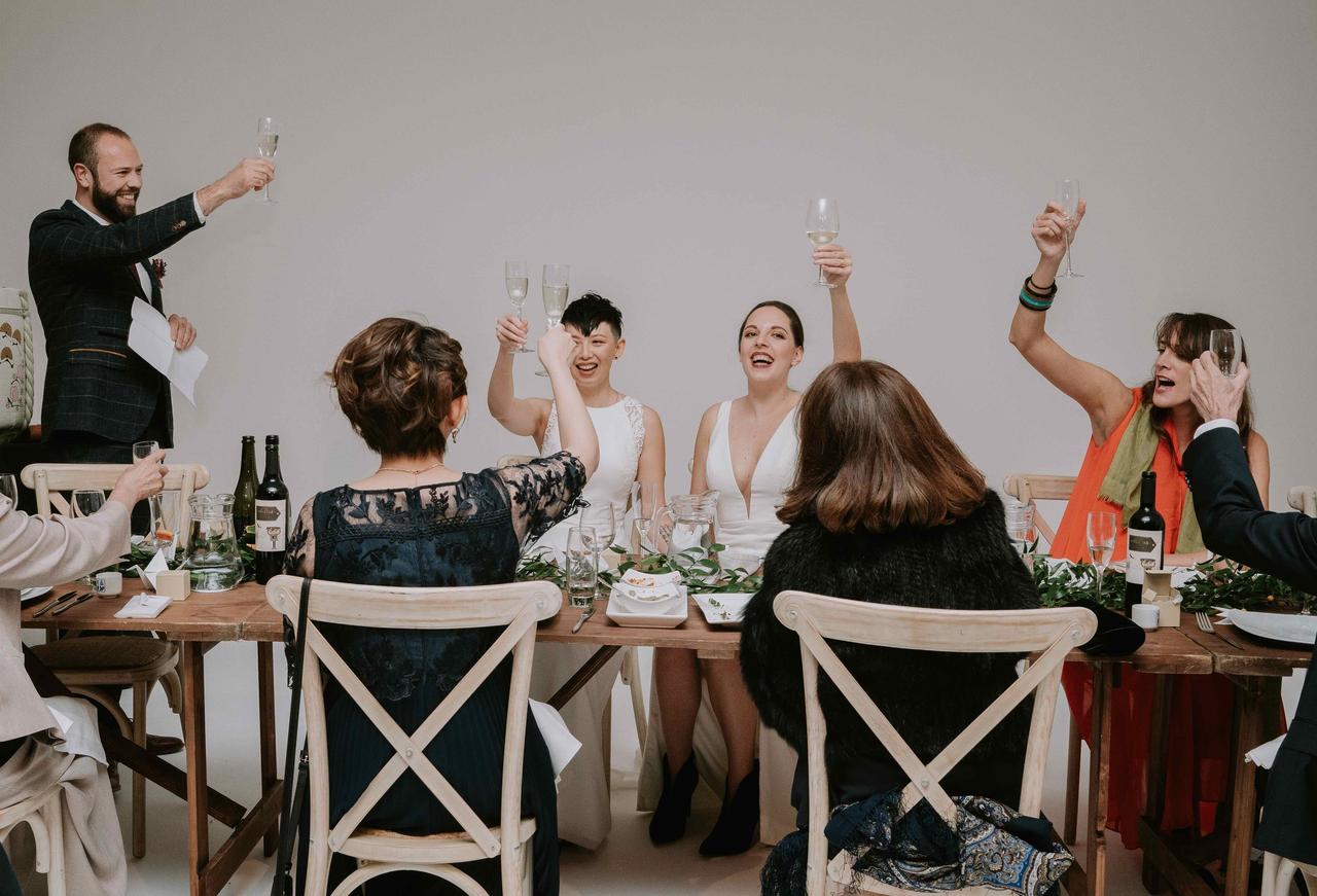 The brides raise a toast at the table with their guests