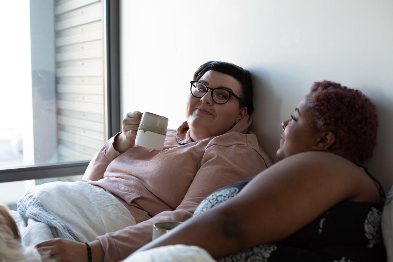 Female same sex couple sitting in bed together drinking tea discussing their relationship