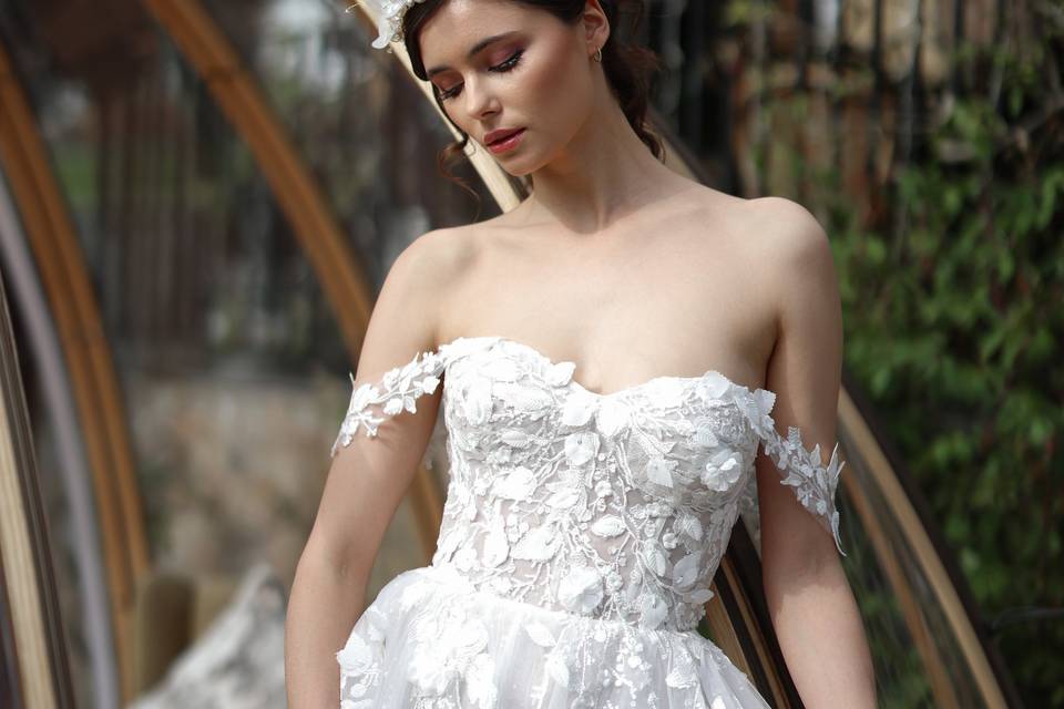 Model wearing a flower crown and a lace off the shoulder wedding dress while holding a bouquet of white flowers