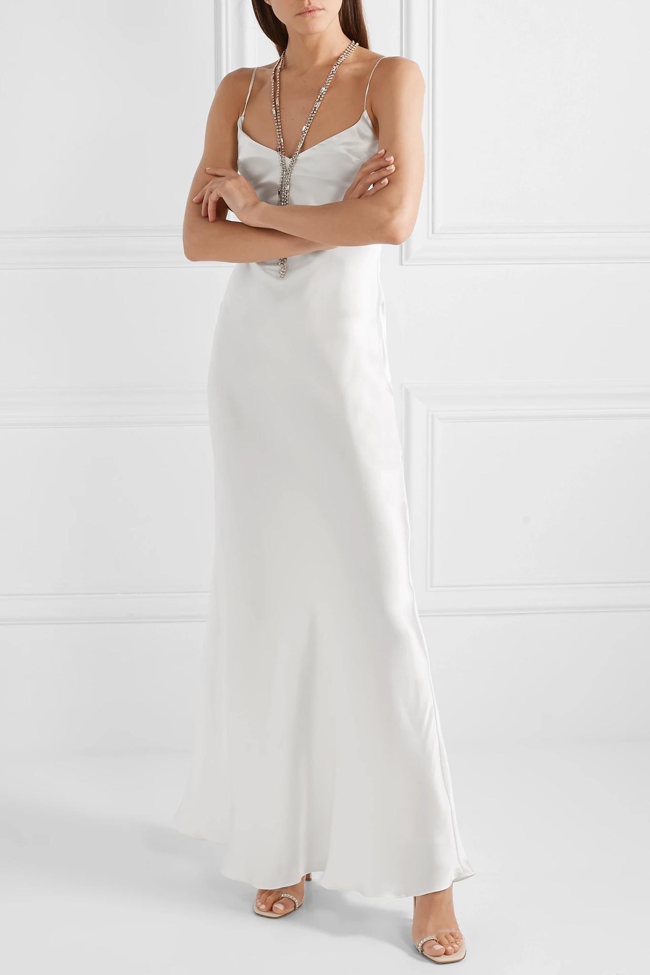 White woman with loose dark hair wearing a white silk slip dress and a chunky sparkly silver necklace