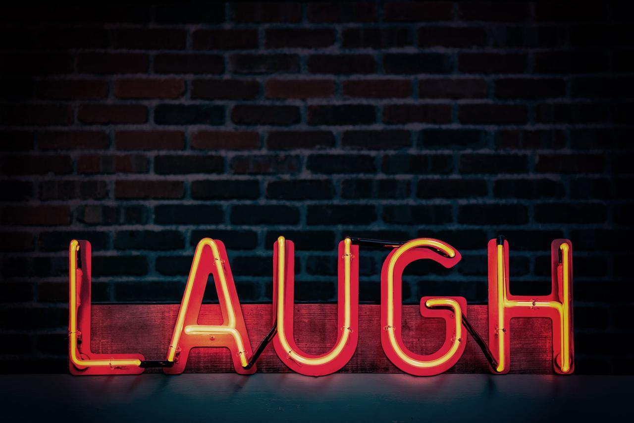 Orange neon laugh sign against a black brick wall
