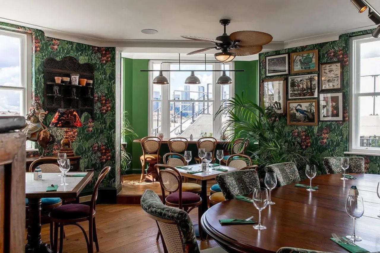 A garden-inspired wedding event room with plant, green pattern wallpaper and large wooden tables