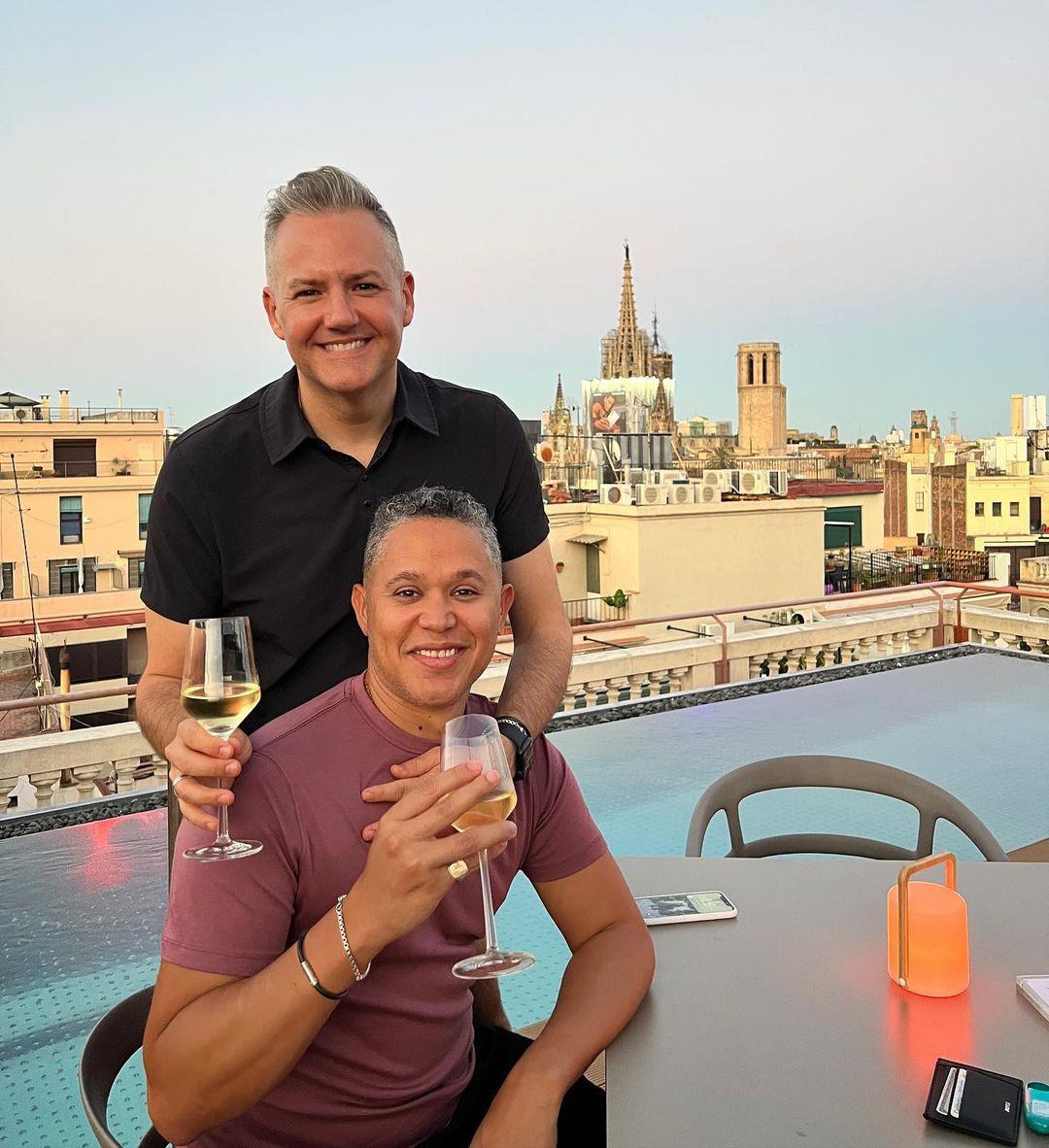 Ross Matthews and his husband smiling holding glasses of wine