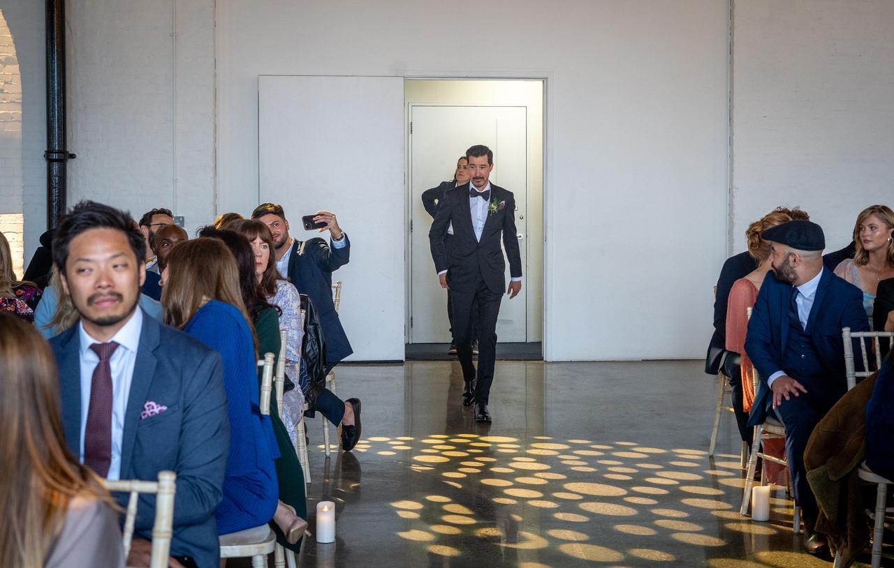 A groom walks down the aisle as the wedding guests look on
