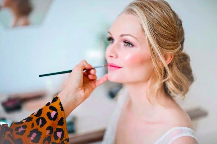 Blonde bride having her lipstick applied with a brush