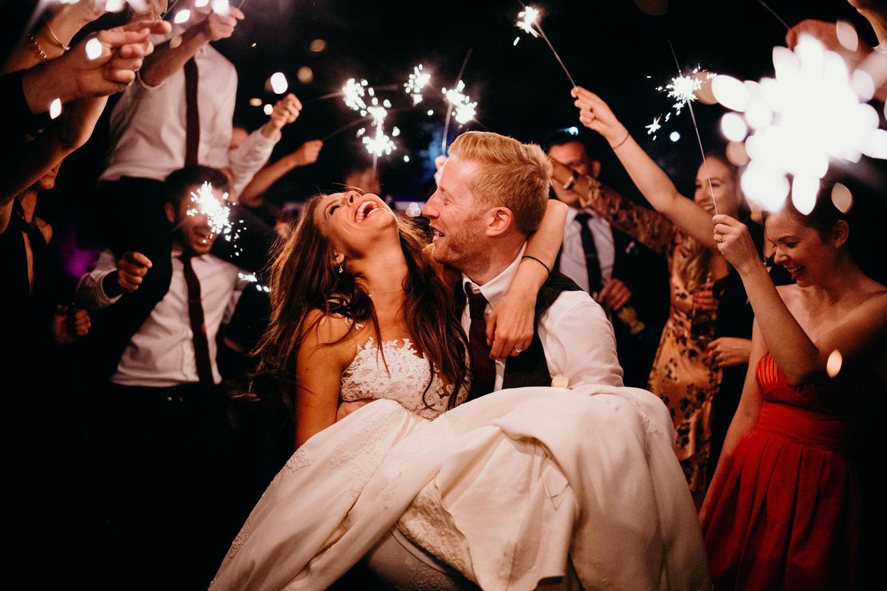 Groom carrying a bride surrounded by wedding guests holding sparklers
