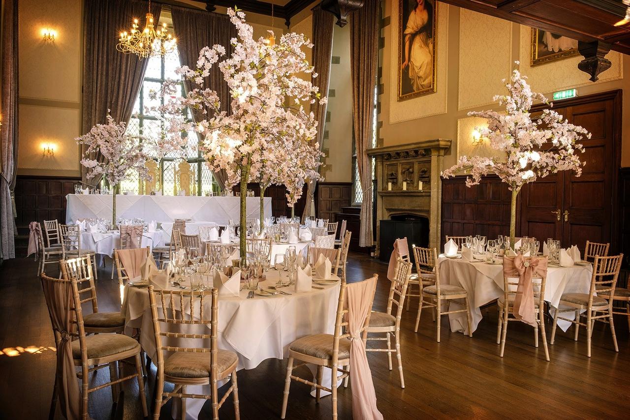 A tall room set up for a meal with cherry blossom centrepieces, rich wooden fixtures, and a stone fireplace