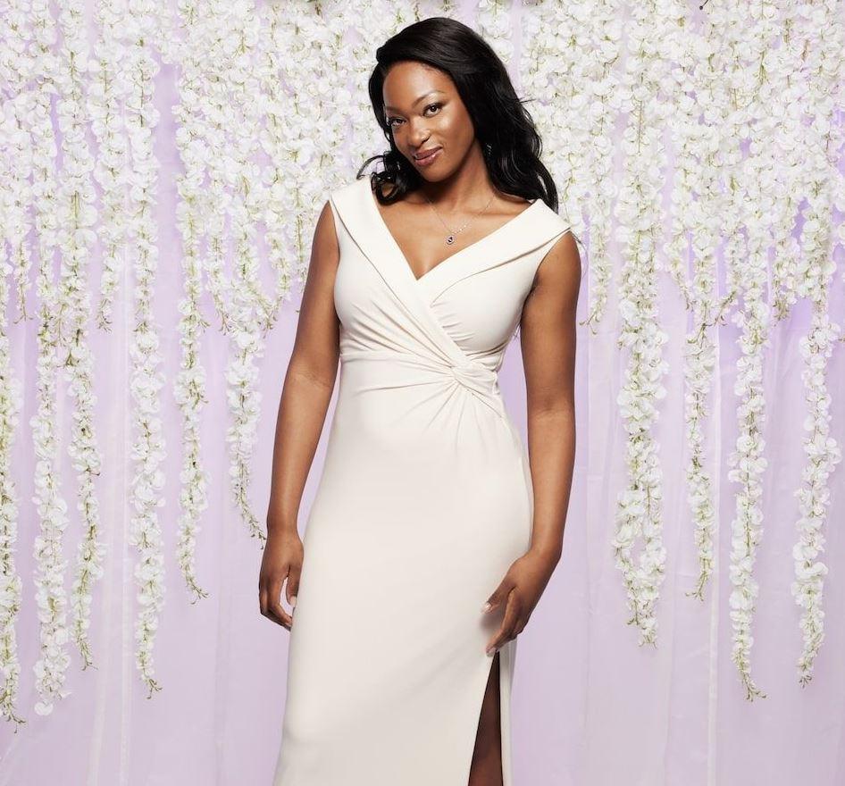 mafs uk 2023 contestant porscha wears a fitted v-neck wedding dress in front of a lilac and white floral backdrop