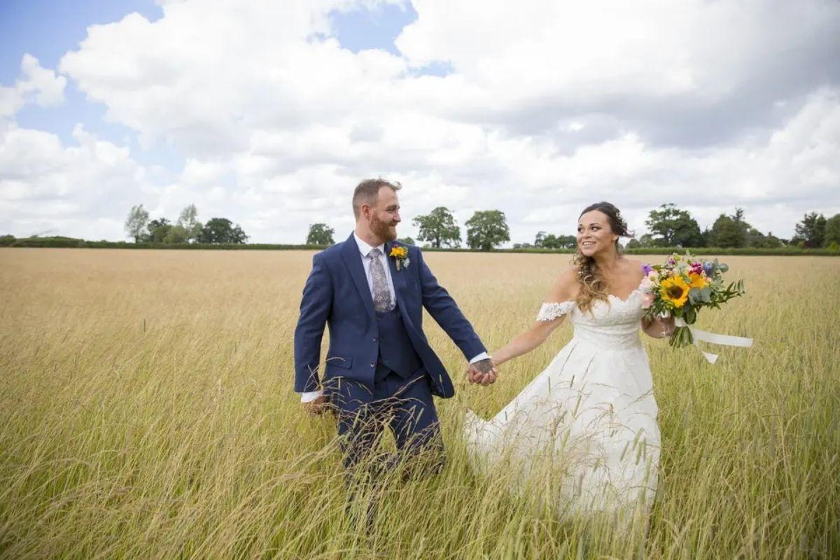 a bride and groom walking and holding hands as they walk through a field of green grass on a clear blue day