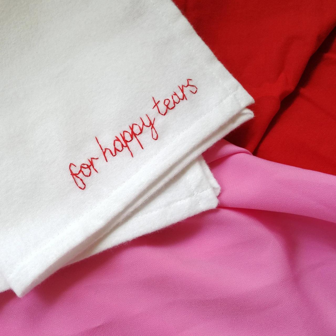 A white cotton hanky that reads 'for happy tears' in red embroidery.
