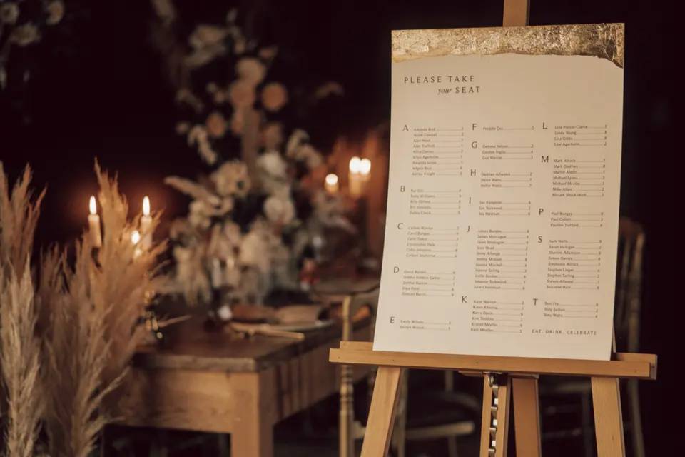 a gold foil and white wedding table planner with guests names in alphabetical order in a dimly lit room