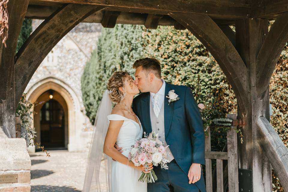 A bride and groom kiss at the church gates