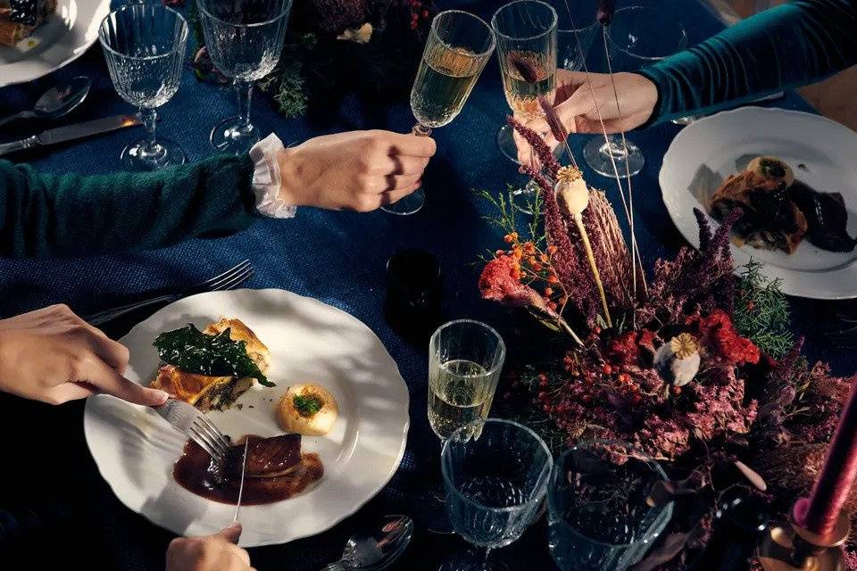 People cheers champagne while others tuck into a vegan plate on a table with a navy tablecloth and a floral display