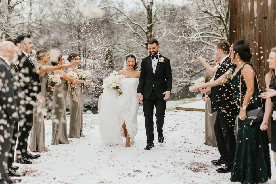 A bride and groom walking through the snow through an aisle of people throwing confetti