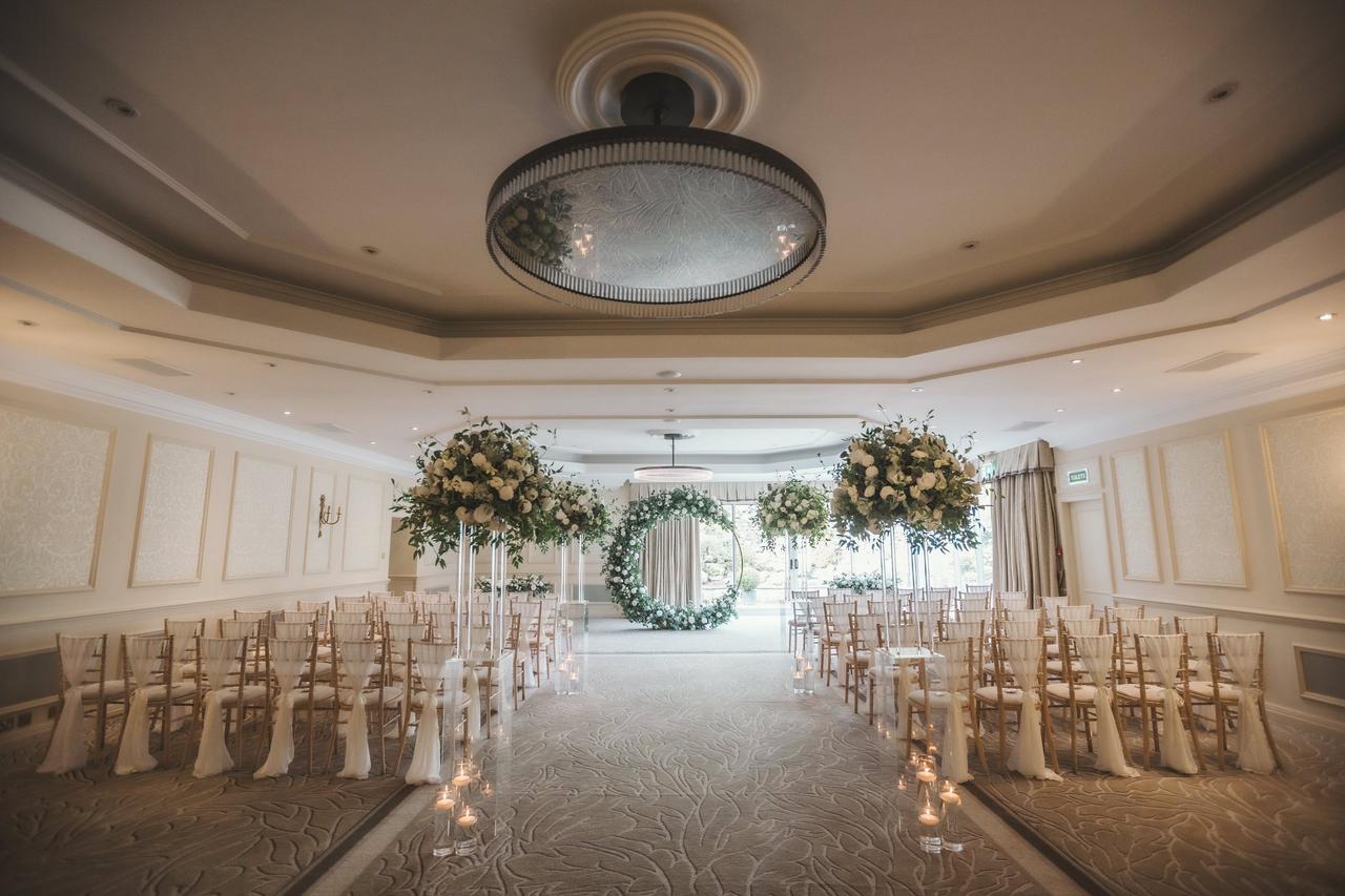 Modern, luxurious wedding ceremony room with a floral hoop at the end and tall floral arrangements along the aisle